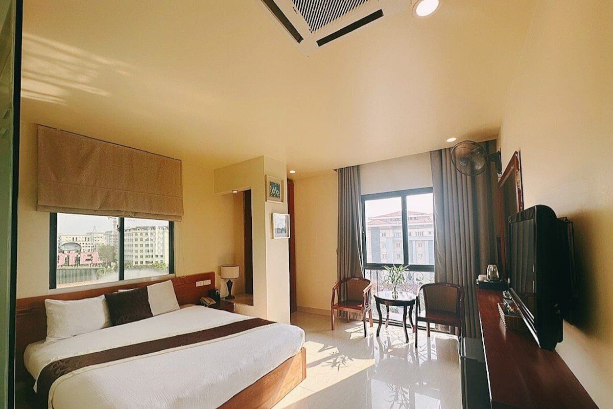 Habitación de hotel con una cama grande, un escritorio, una silla, un televisor y una ventana con vistas a edificios.