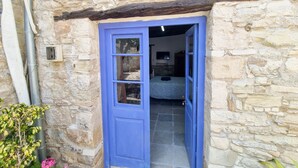 Un bâtiment en pierre avec une porte bleue, une pièce visible avec un lit et un mur en pierre.
