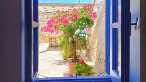 Une porte ouverte donne sur une cour intérieure où se trouvent un palmier et des plantes en pot.