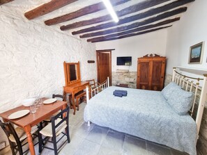 Un dormitorio con cama, armario de madera, escritorio con silla, espejo y televisor en la pared.