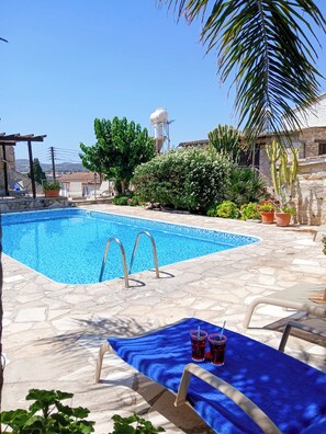 Una piscina con borde de mosaico azul, rodeada de baldosas de piedra y plantas en macetas.