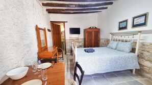Une chambre à coucher avec un lit, une armoire en bois, une table à manger avec des chaises et un mur blanc orné d’un miroir.