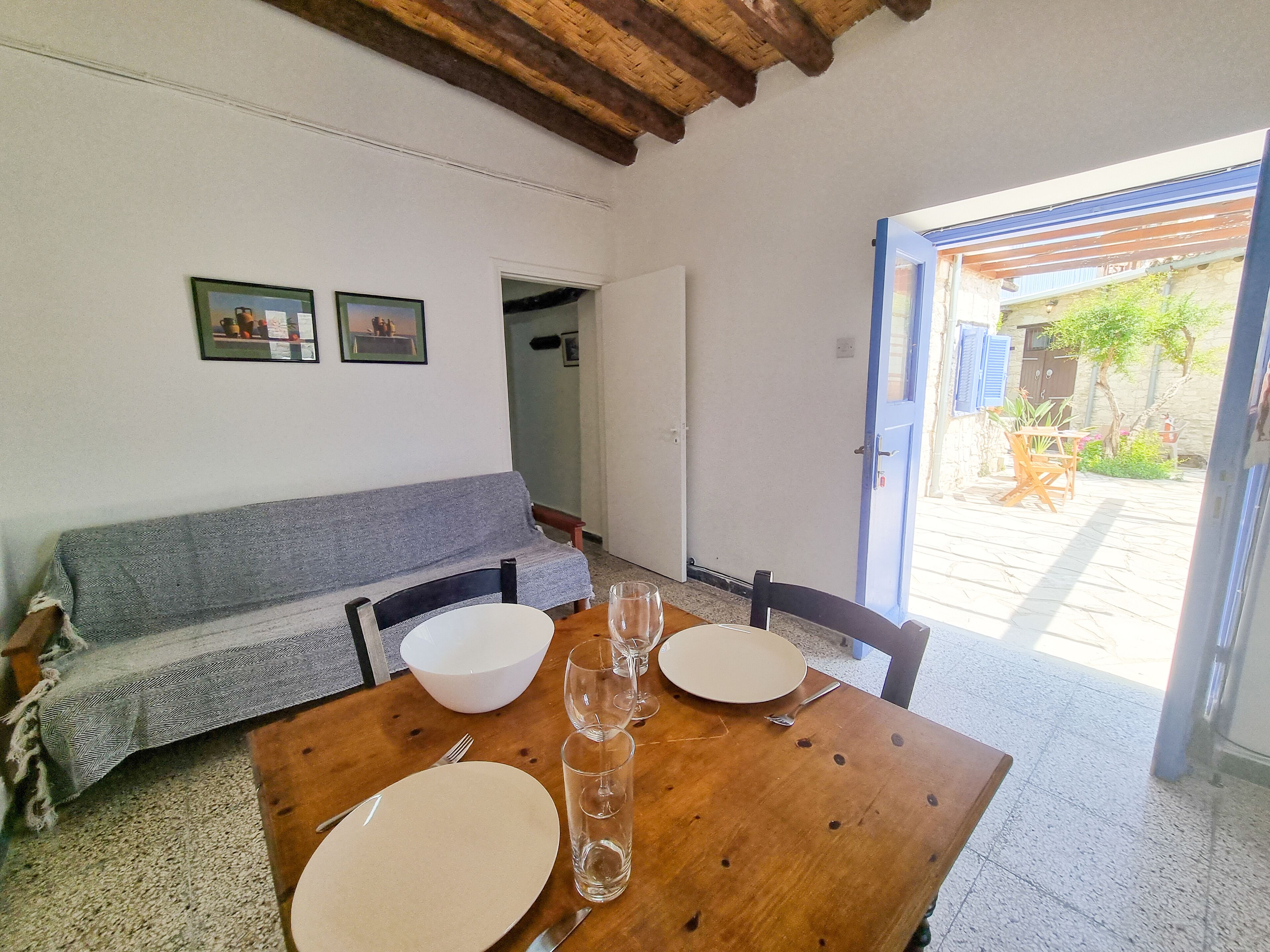 Un coin repas avec une table en bois dressée pour quatre personnes, un canapé gris et une porte donnant sur l’extérieur.