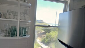 Una cocina con un ventanal amplio, un refrigerador blanco y estantes con diferentes tipos de cristalería.