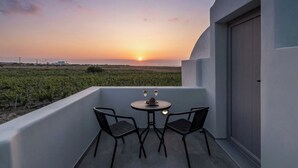 Un balcon avec une table et des chaises, donnant sur un vignoble et offrant une vue sur le coucher du soleil.