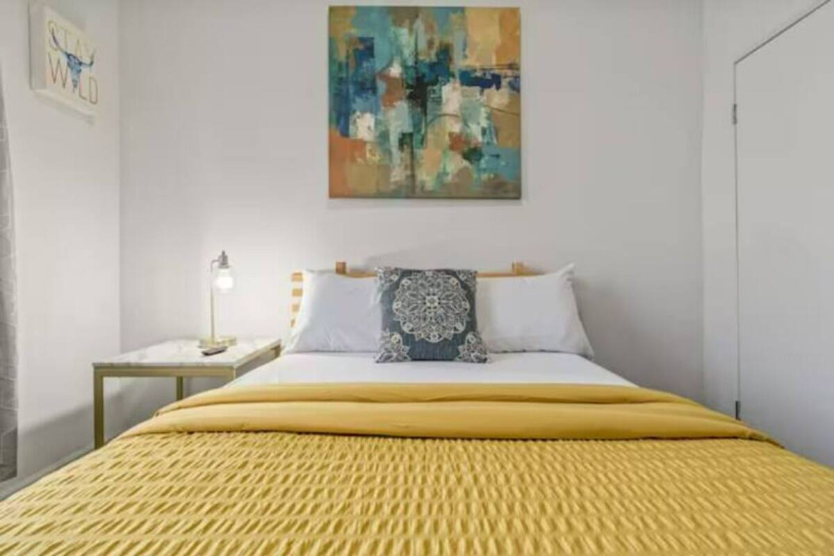 Una habitación de hotel con una cama, una mesita de noche, una lámpara y un cuadro en la pared.