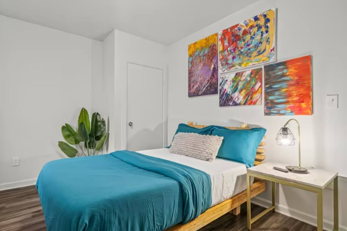 Un dormitorio con cama, una mesita de noche, una lámpara y una planta en maceta.