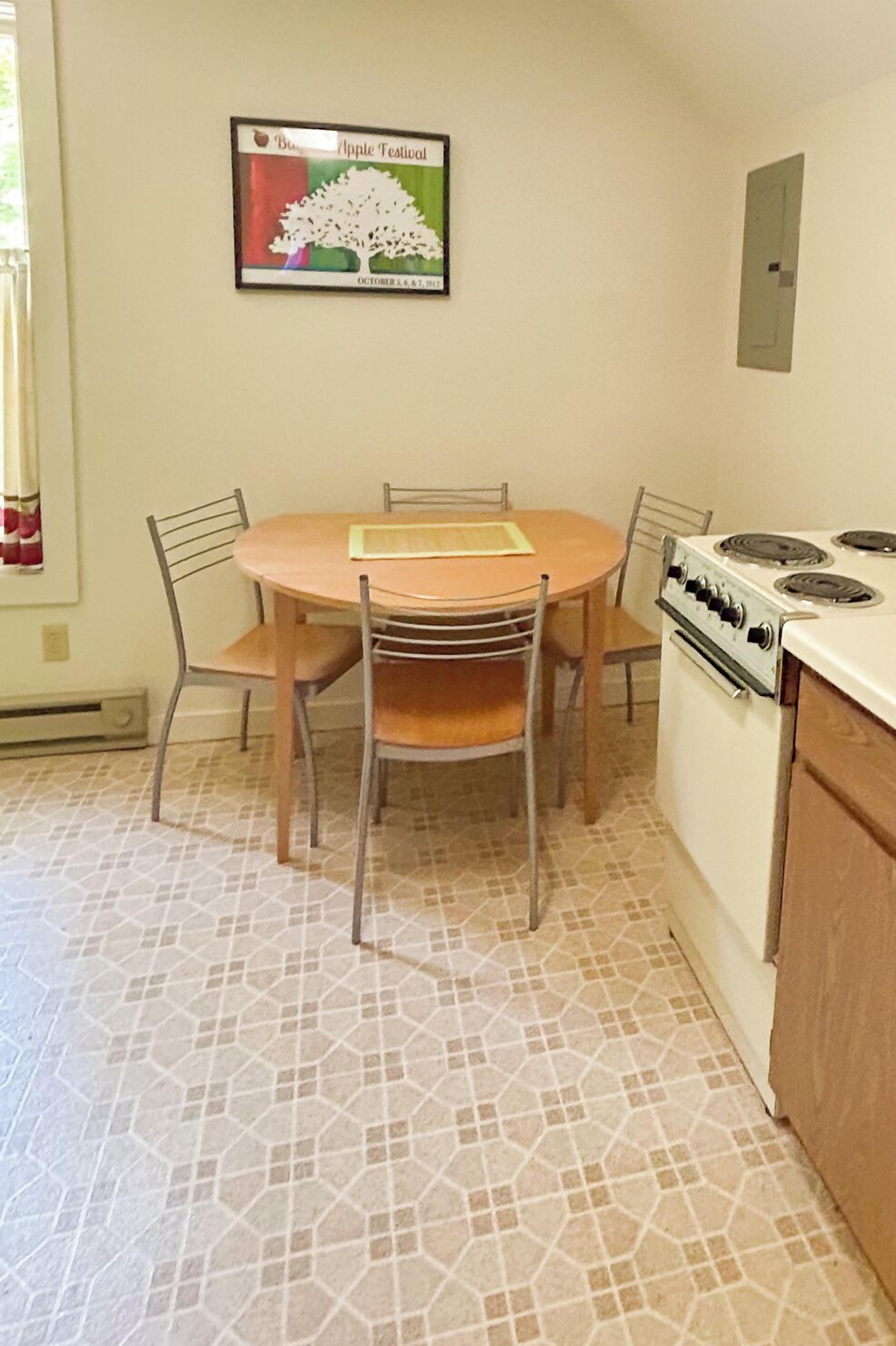 A dining area with a round table, four chairs, and a stove.