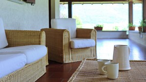 Un conjunto de sofá y sillones de mimbre con cojines blancos, una mesa trenzada y dos tazas blancas sobre un tapete tejido.
