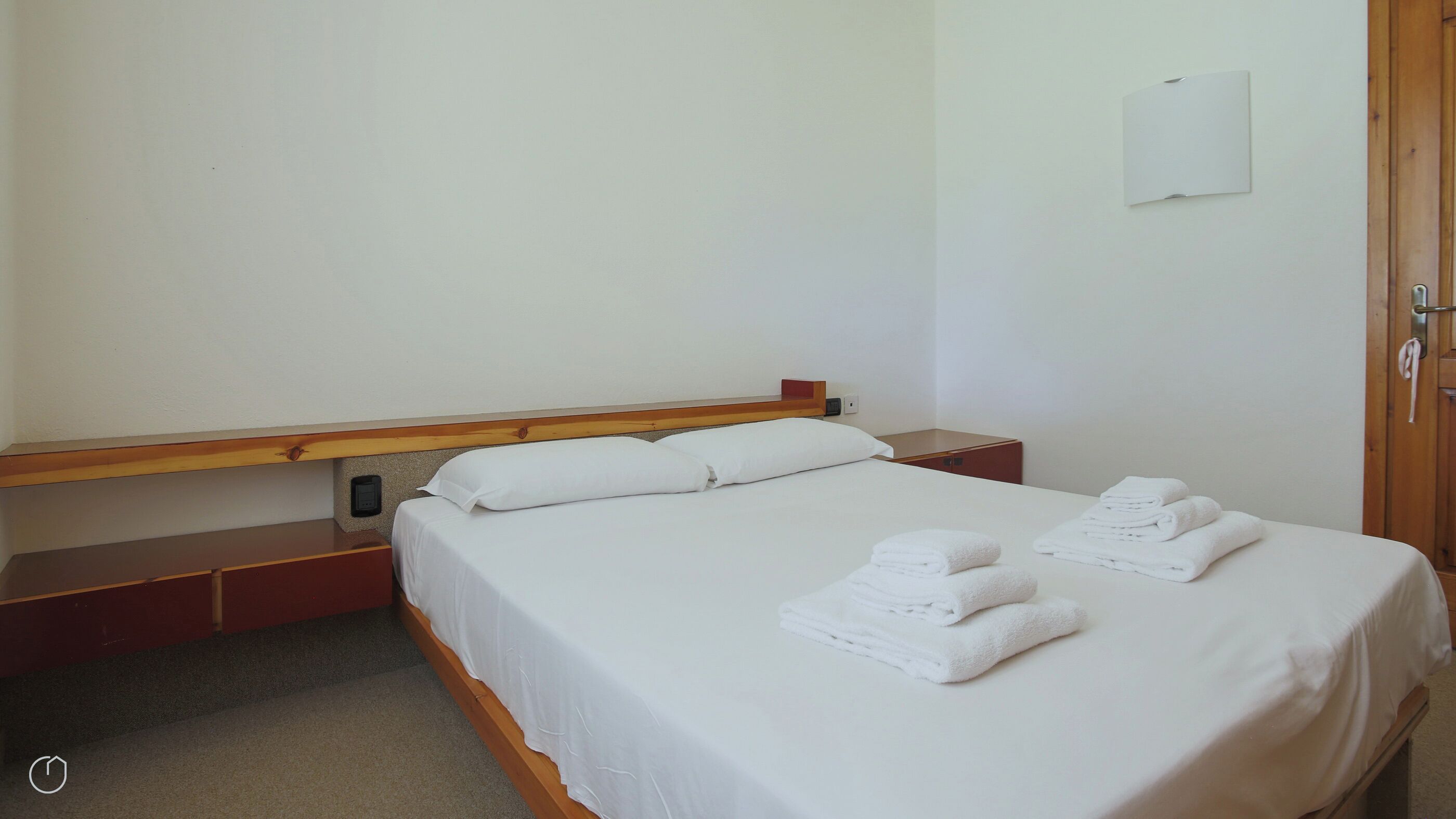 Hotellihuone, jossa on yksi sänky, puinen pääty, yöpöytä ja pieni puinen kaappi.