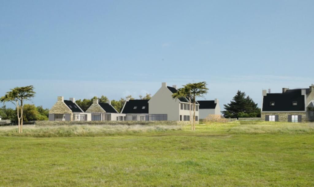 A row of modern houses with sloped roofs and stone foundations, set in a grassy field with trees in the background.