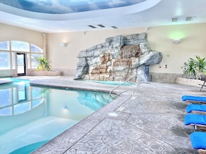 Piscina interna com parede de pedra e espreguiçadeiras azuis.