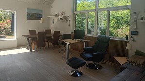 A modern room with a dining area, a computer desk, a green armchair, and large windows offering a view of greenery. - 3 bedroom private vacation home in silkeborg (Silkeborg)