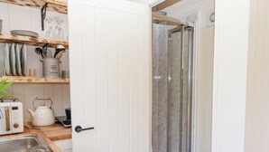 Une cuisine compacte équipée d’un évier, d’un grille-pain, d’une bouilloire et d’une cabine de douche en verre.