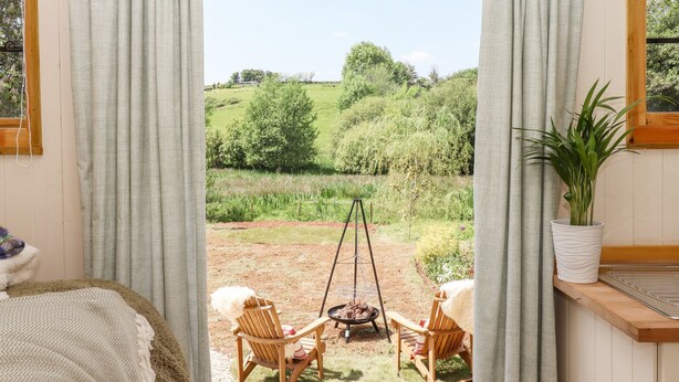 Une pièce avec vue sur un champ verdoyant et des arbres, une chaise en bois, une petite table et une plante en pot.