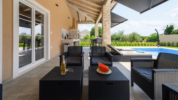 An outdoor patio with wicker furniture, a bottle of wine, and a watermelon on a table. - Luxury Villa Istra Maruzini with private pool in Rovinj,  Istria (Maružini)