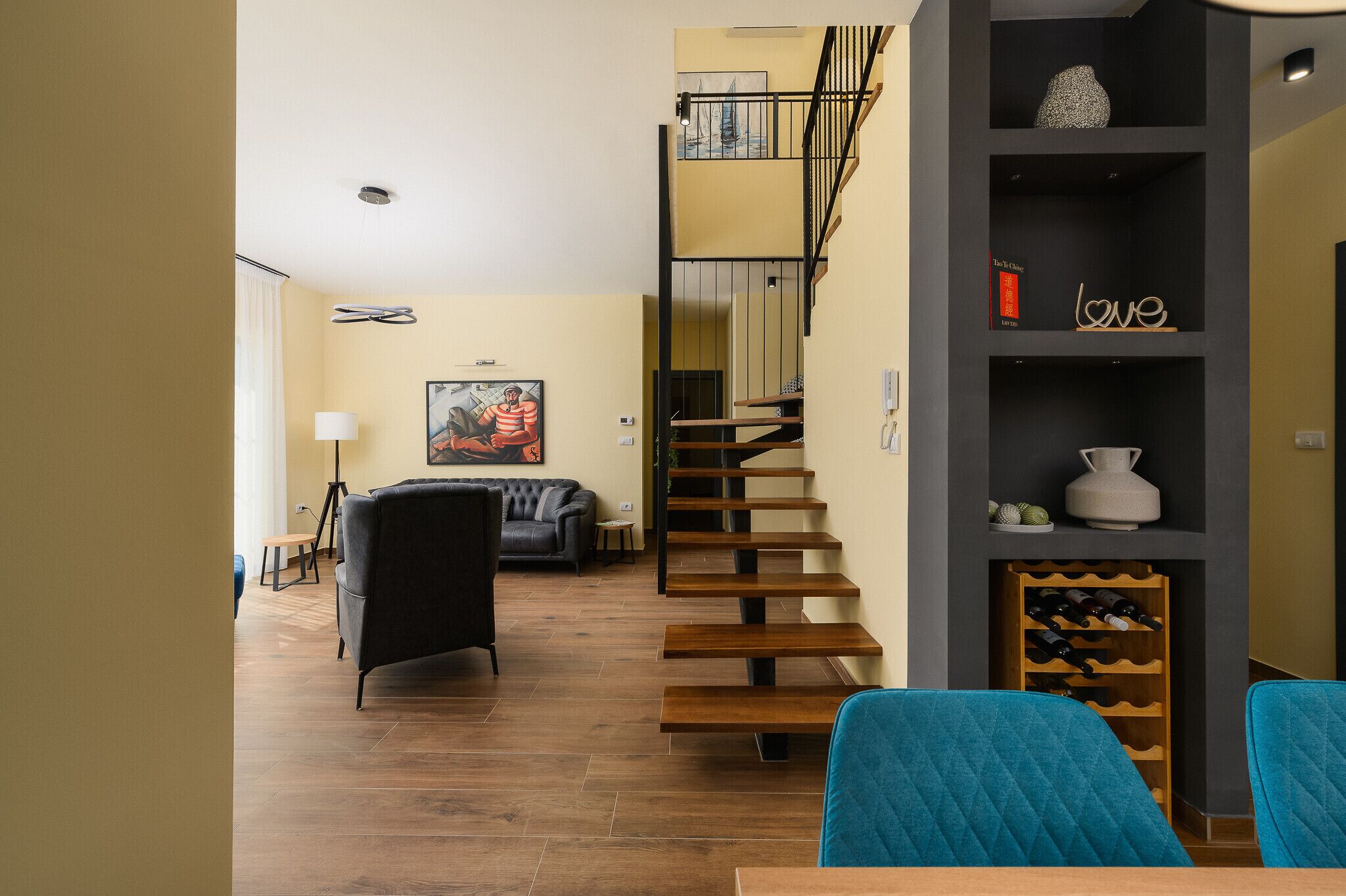 A modern living room with a staircase, a black sofa, and a wine rack.