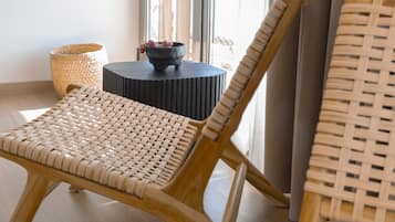Una habitación con una silla de mimbre, una mesita redonda con un cuenco y un caballete de mimbre.
