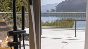 A bathtub with a faucet, a window with a view of a lake and trees, and a metal railing. - Malates Slow Boutique Hotel (Foz)