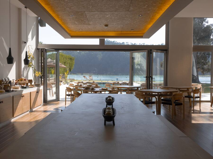 A modern kitchen with a large island, wooden furniture, and a view of the sea.