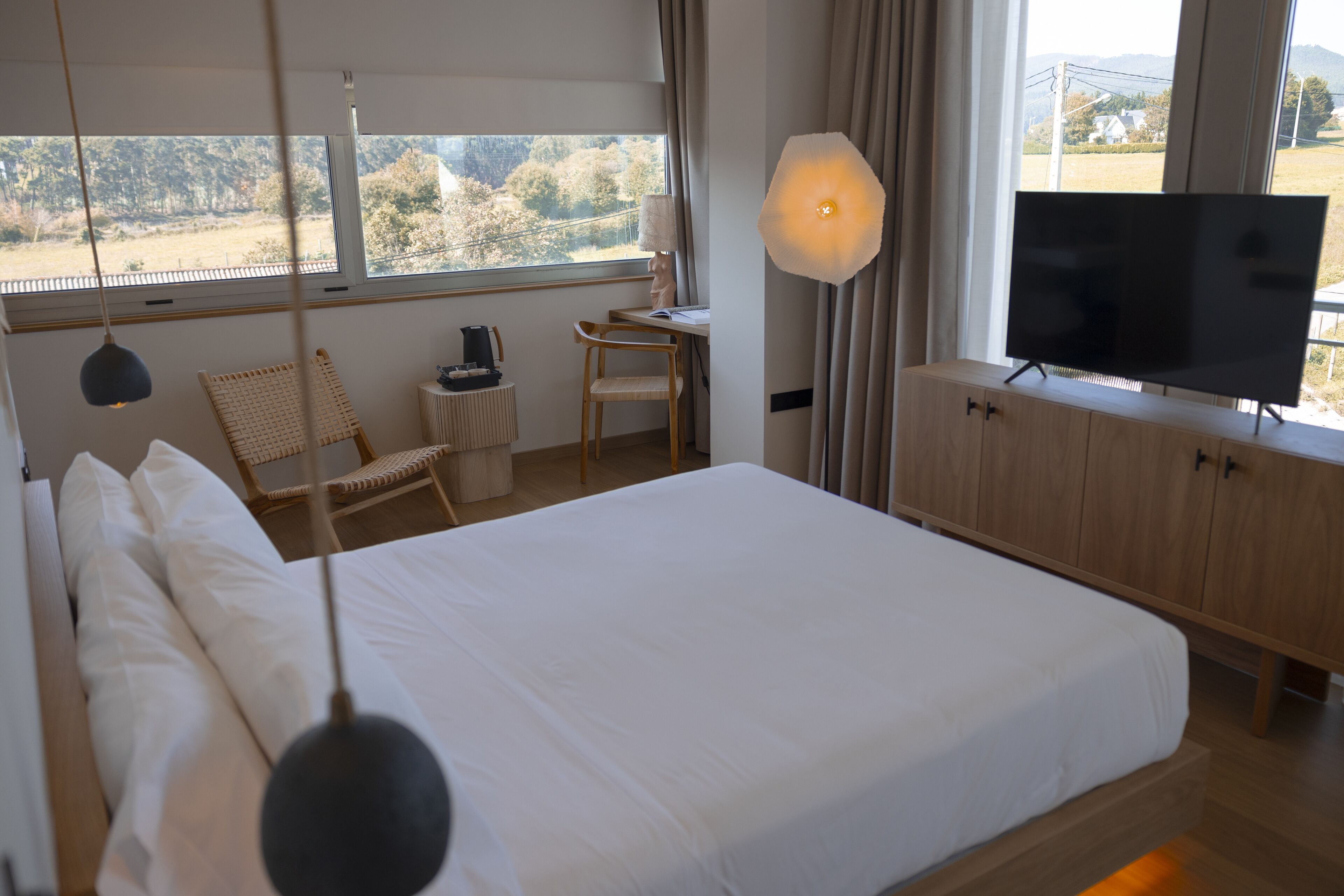 A hotel room with a large bed, a television, a desk with a lamp, and a view of the outdoors.