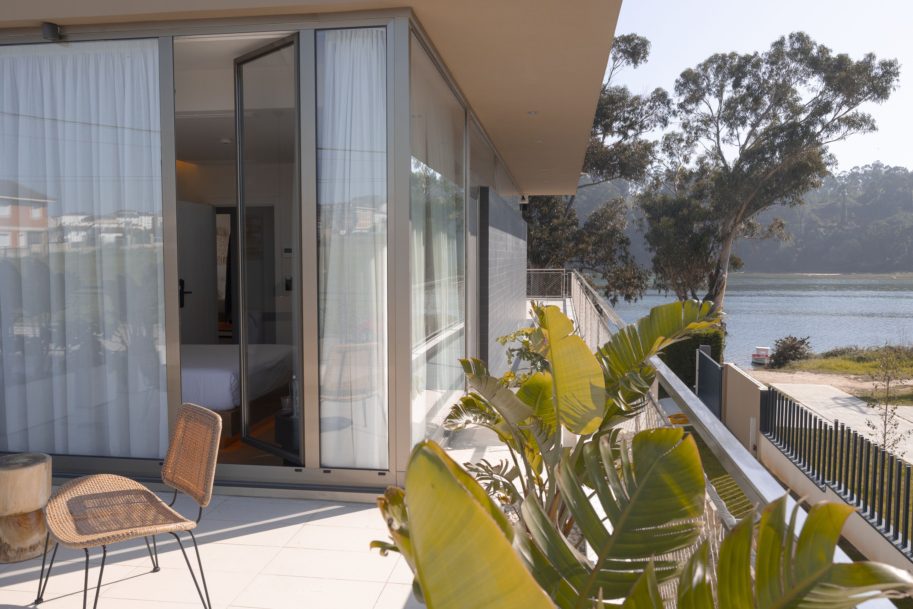 Een moderne hotelkamer met een schuifglazen deur die uitkomt op een balkon met uitzicht op een meer en bomen.