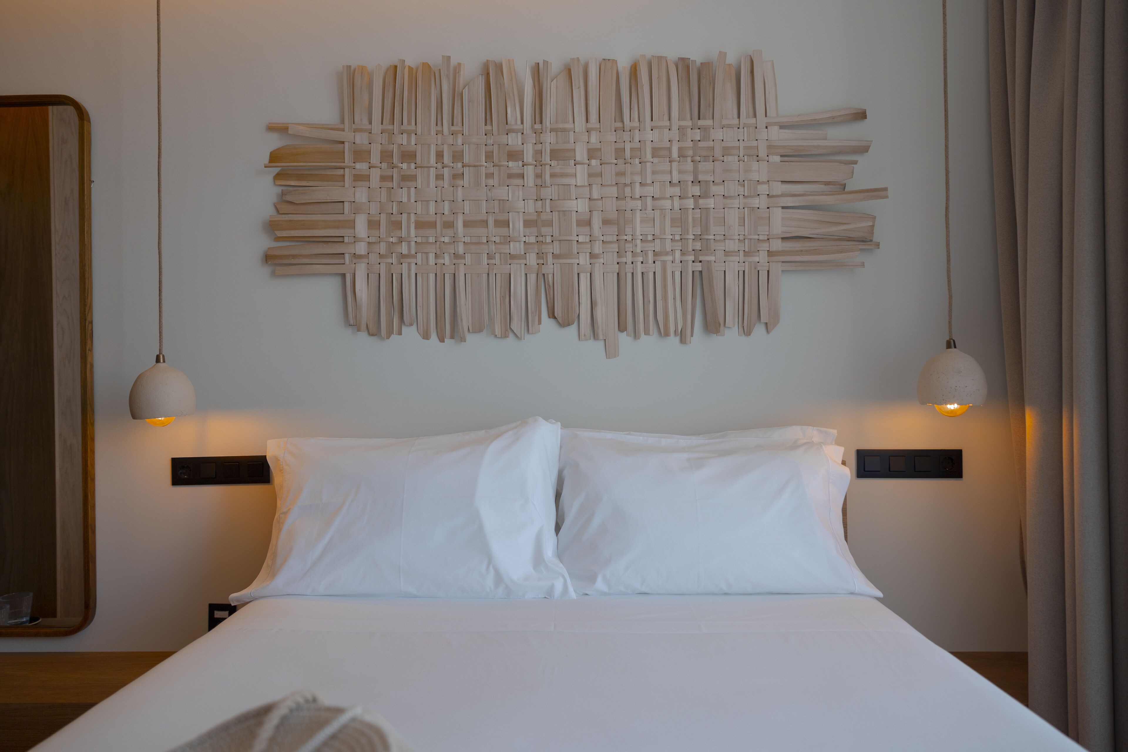 Una cama bien hecha con sábanas blancas, una obra de arte abstracto colgada en la pared y dos lámparas colgantes.