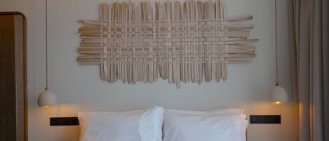 Una cama bien hecha con sábanas blancas, una obra de arte abstracto colgada en la pared y dos lámparas colgantes.