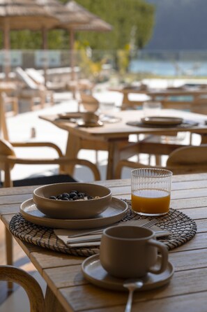 A wooden table with a bowl of blueberries, a glass of orange juice, and a cup and saucer. - Malates Slow Boutique Hotel (Foz)