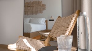 A modern hotel room with a bed, a woven chair, a glass table, and a bottle. - Malates Slow Boutique Hotel (Foz)