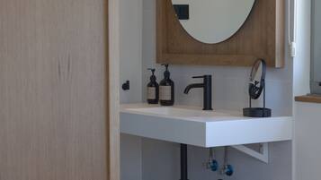 Un baño moderno con tocador de madera, espejo redondo y lavamanos. Hay toallas y artículos de aseo en la encimera.