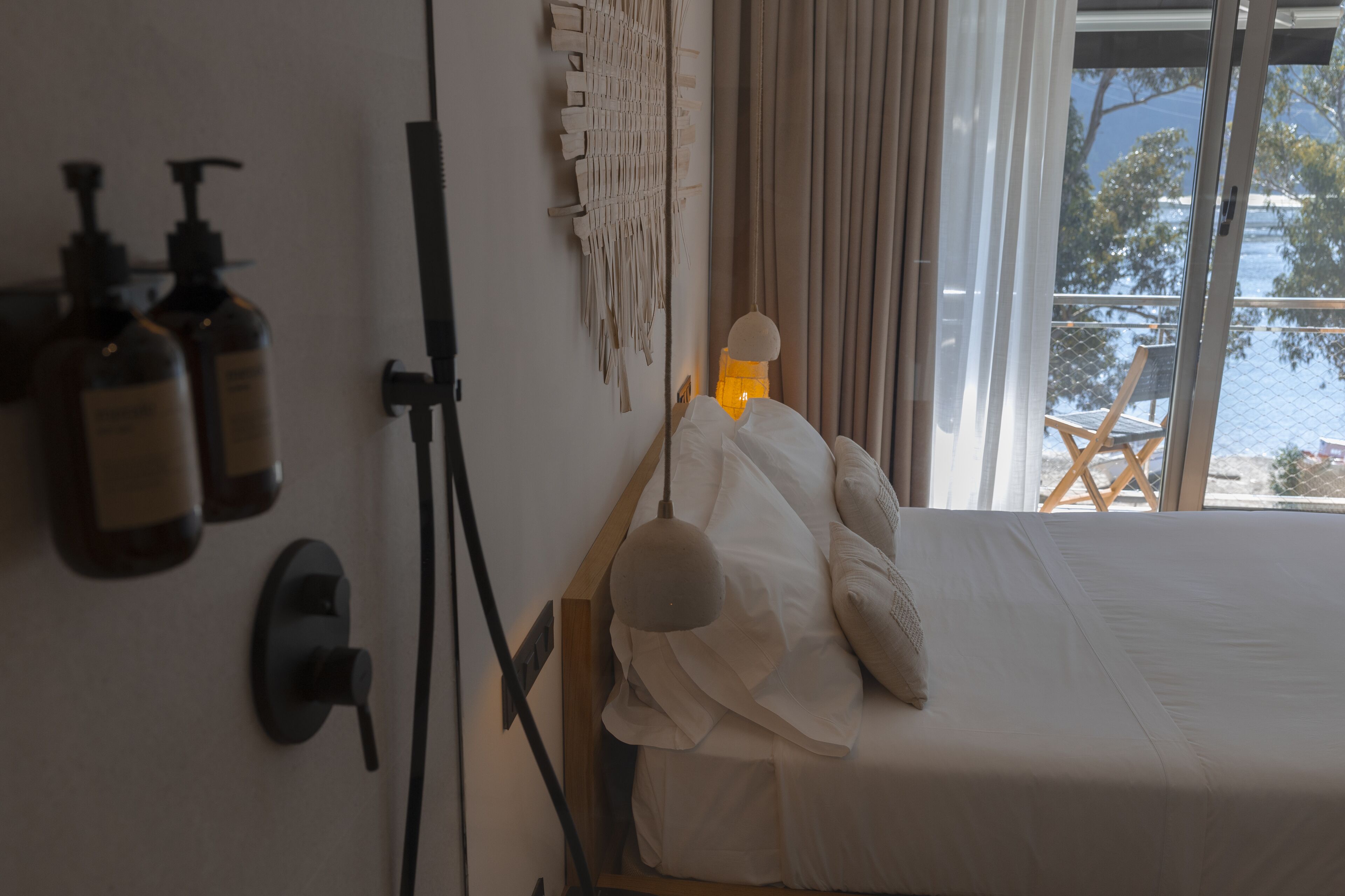 Un dormitorio con una cama, un adorno macramé en la pared y una ventana con vistas a un balcón y árboles.