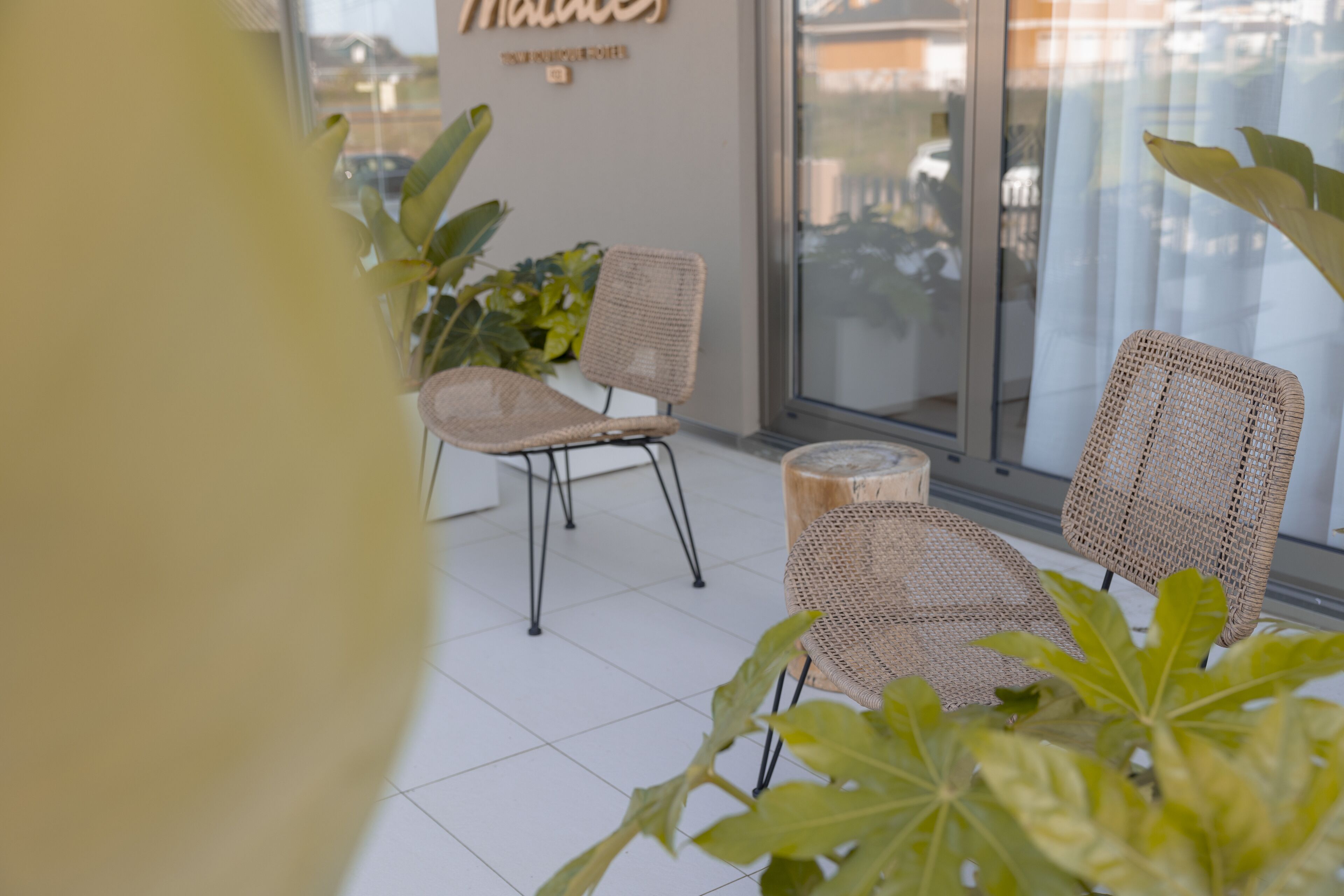 Een zithoek met rieten stoelen en een houten krukje, een potplant en een bord op de muur.