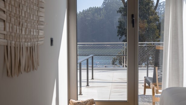 A room with a large sliding glass door leading to a balcony with a metal railing, a view of the sea, and a woven basket on the floor. - Malates Slow Boutique Hotel (Foz)