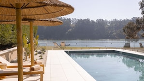 A swimming pool with a view of a lake, surrounded by lounge chairs and a thatched umbrella. - Malates Slow Boutique Hotel (Foz)