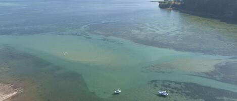 Vista aérea de una zona costera con aguas claras, barcos y una orilla con edificios.