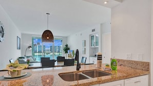 Una cocina moderna con encimeras de granito, un lavamanos de acero inoxidable y vistas a la ciudad.