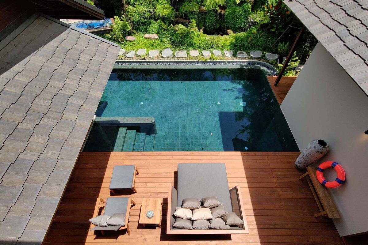 A rooftop pool with a wooden deck, lounge chairs, a small table, and a life ring.