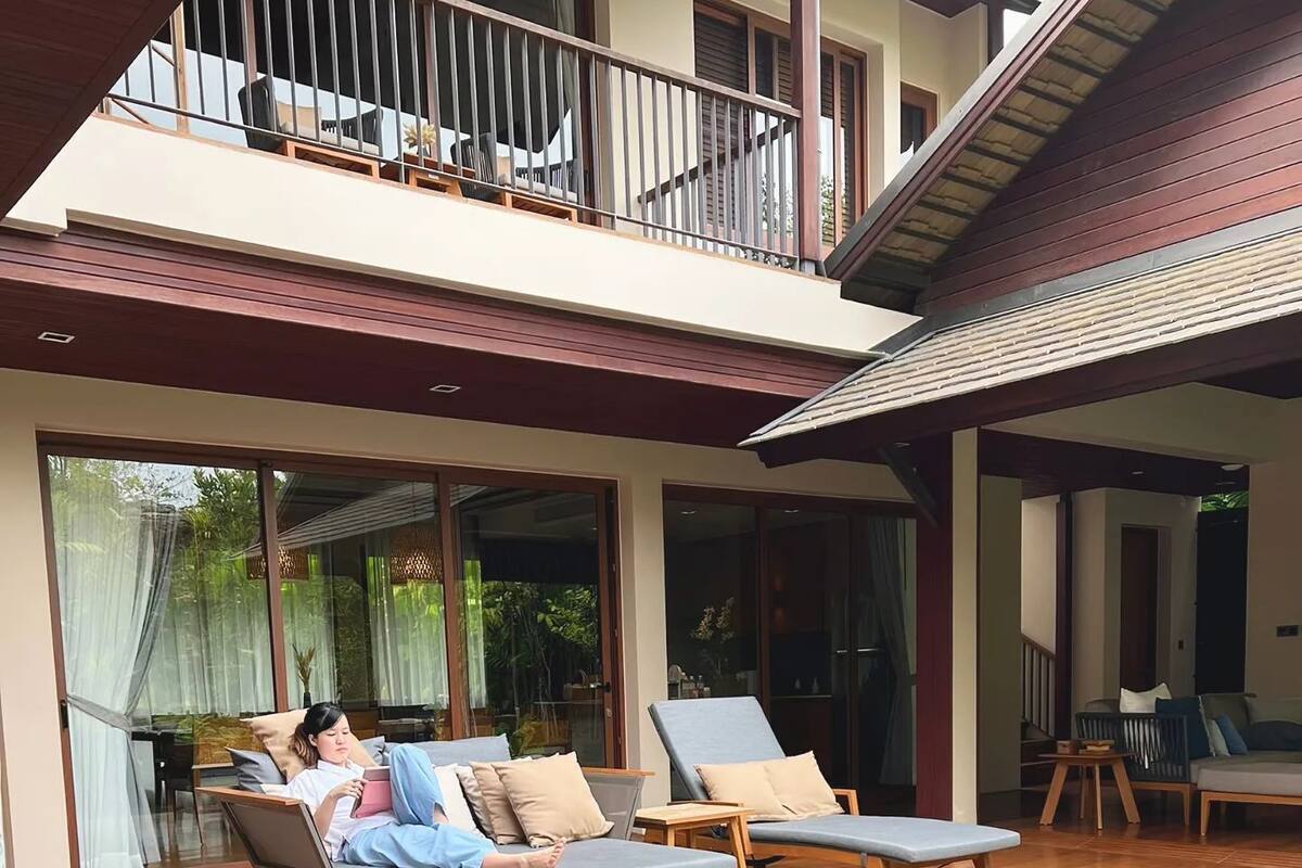 A poolside area with two lounge chairs and a person reading a book.