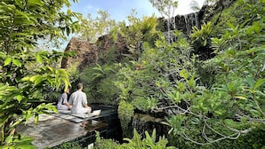 A serene outdoor area with a stone bridge over a small stream, surrounded by lush greenery and a rocky backdrop. - Rarin Villas (Chiang Mai)