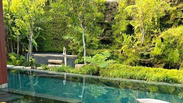A poolside area with a tablet displaying a property listing, surrounded by lush greenery and a clear pool. - Rarin Villas (Chiang Mai)