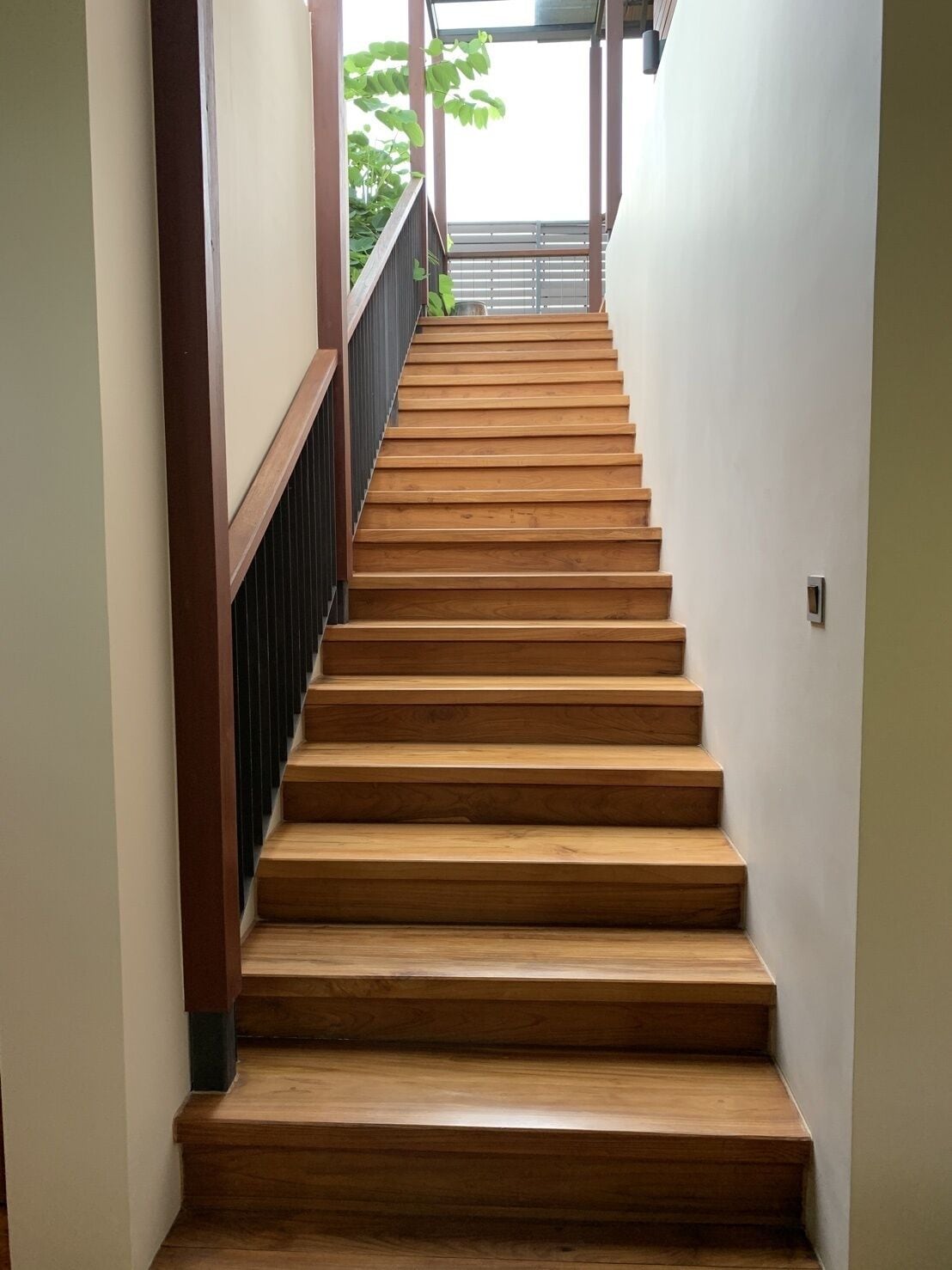 A wooden staircase with a handrail, leading to a covered outdoor area.