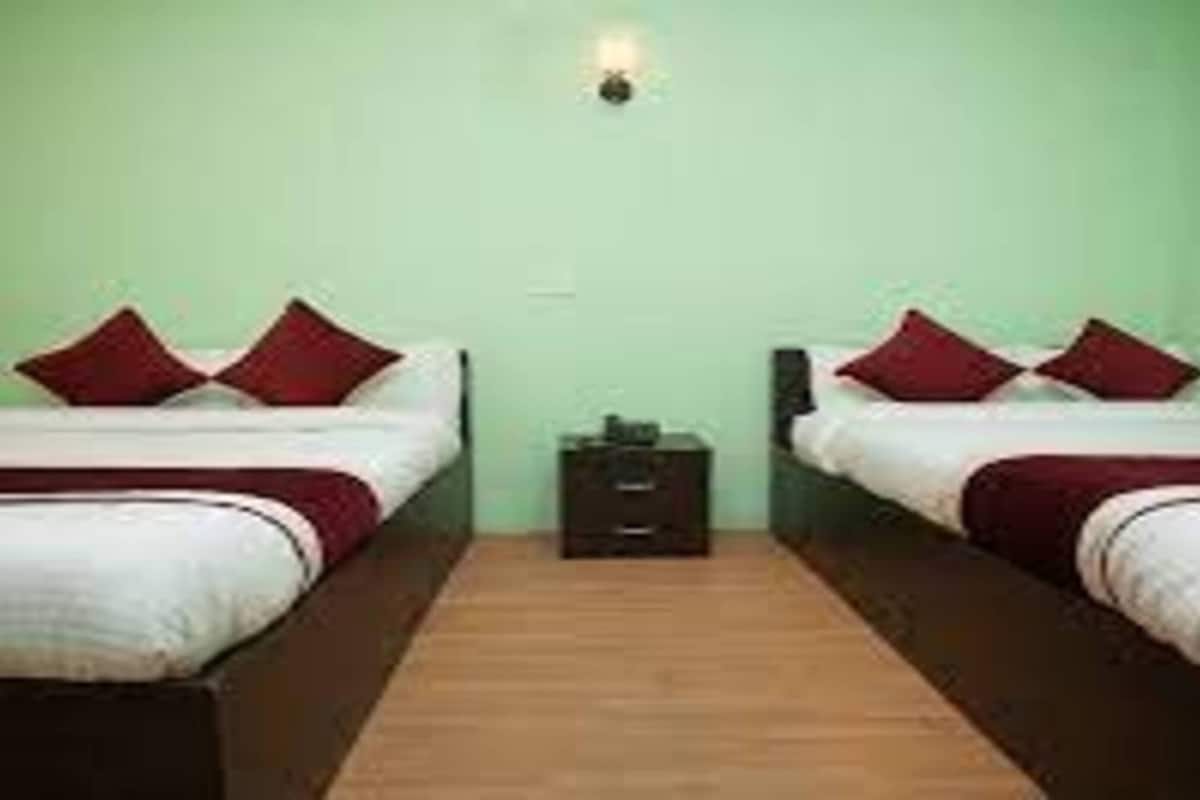 Una habitación con dos camas, cada una con almohadas rojas y ropa de cama blanca, frente a una pared verde.