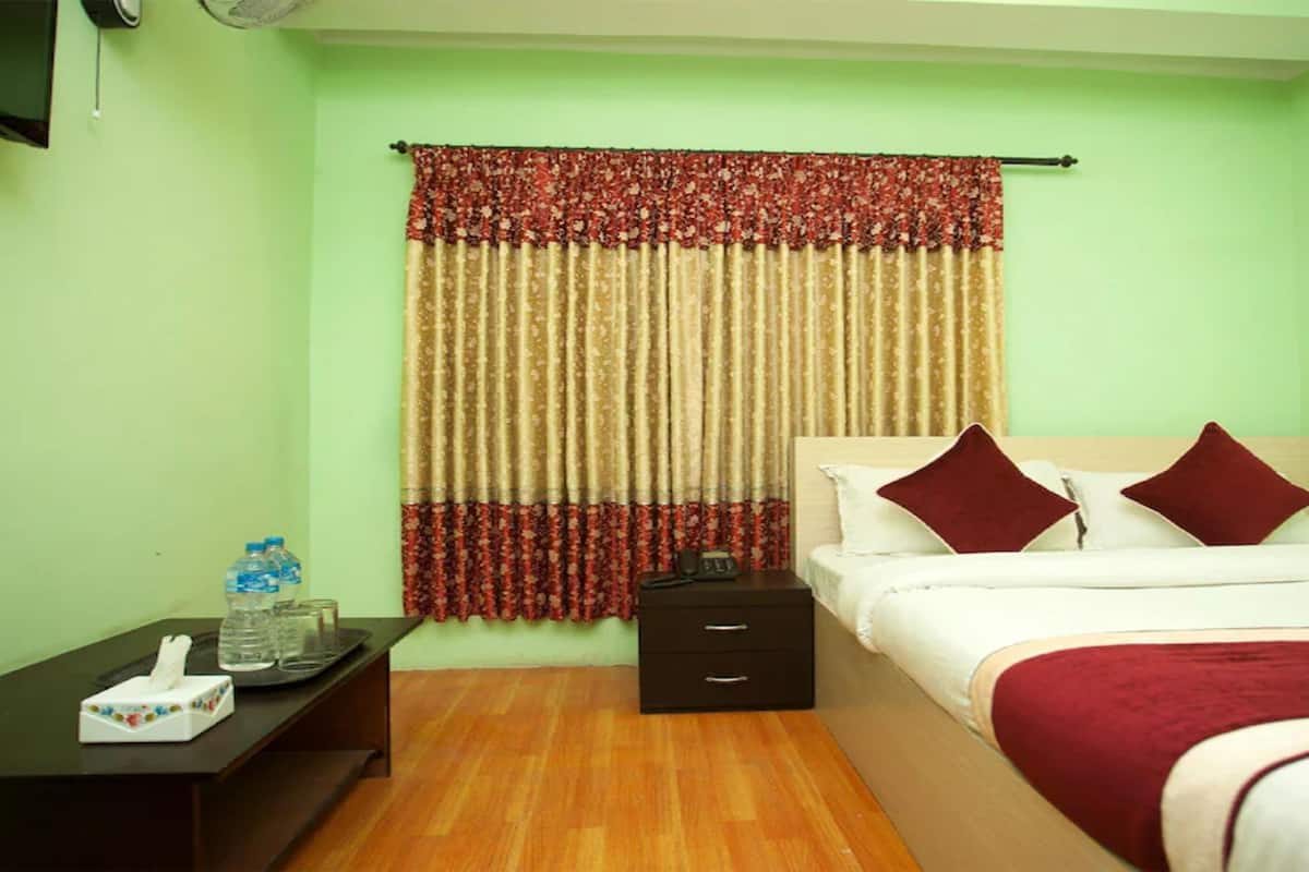 Una habitación de hotel con una cama, una mesita de noche, un escritorio y una ventana con cortinas.