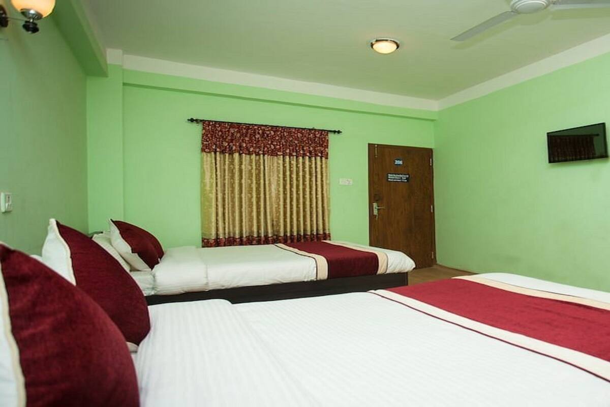 Habitación de hotel con dos camas, ventilador de techo, televisión y puerta que da a un baño.