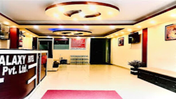 Un hall d’hôtel avec un comptoir d’accueil portant l’inscription « GALAXY Pvt. Ltd. » et un tapis rouge menant à l’entrée.