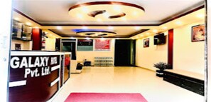 Un hall d’hôtel avec un comptoir d’accueil portant l’inscription « GALAXY Pvt. Ltd. » et un tapis rouge menant à l’entrée.