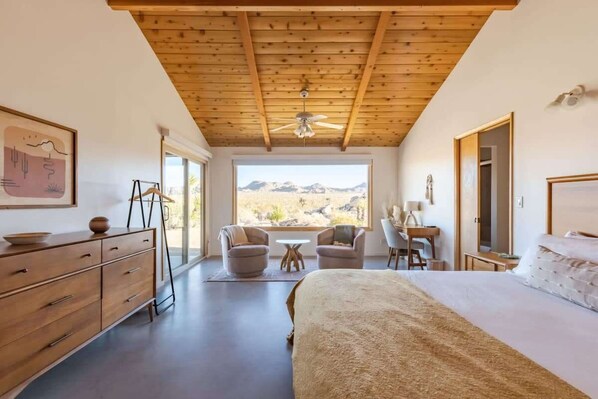 Een slaapkamer met een groot bed, een bureau, twee stoelen, een plafondventilator en uitzicht op de woestijn.