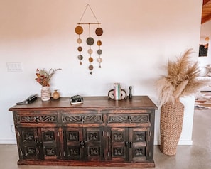 Un meuble en bois agrémenté d’objets décoratifs, un ornement mural suspendu et un panier tressé contenant des plumes d’herbe des pampas.