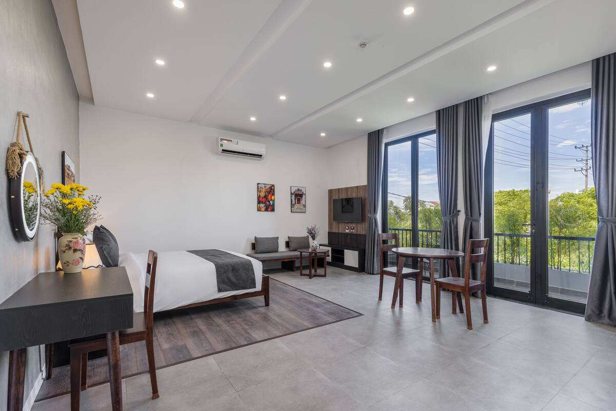 A modern hotel room with a bed, a desk, a chair, a TV, and large windows with curtains.